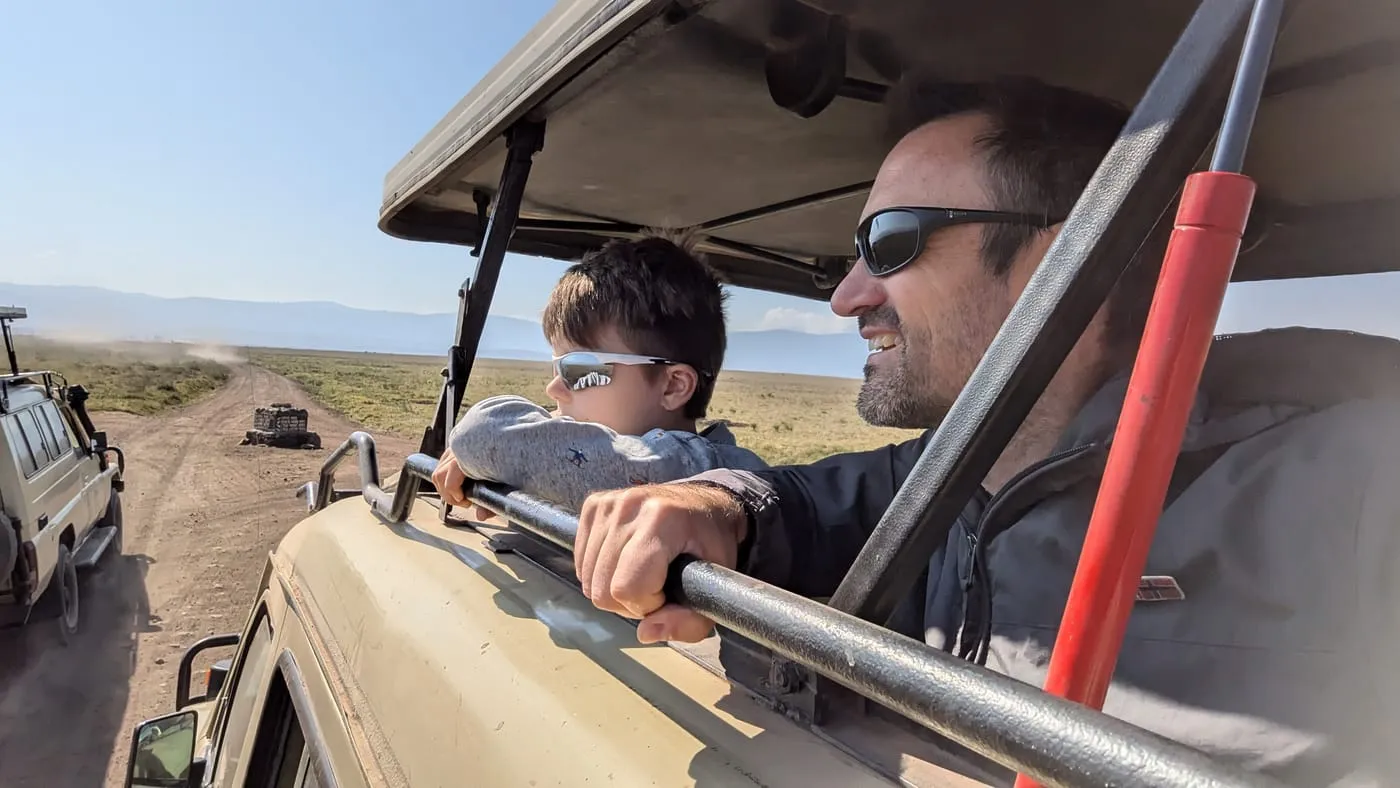 Tim en z’n zoon met zonnebril kijken vanuit een safarijeep over de savanne